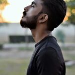 Side view portrait of a bearded man gazing upwards in an outdoor setting with blurred background.